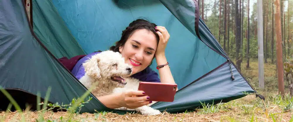 Eine Frau und ein kleiner weißer Hund liegen in einem Zelt, der Eingang ist offen.